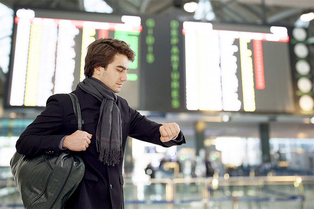Homem olha relógio em aeroporto com voo atrasado
