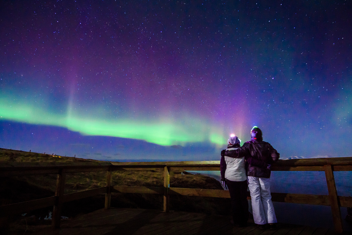 Young adventurist couple hugged while gazing in the dark night sky under the spectacular celestial lights Aurora Borealis, which makes Iceland popular spot for tourist willing to witness one of the greatest natural phenomenon. Shot with Canon EOS, wide angle lens, f2.8, long exposure.