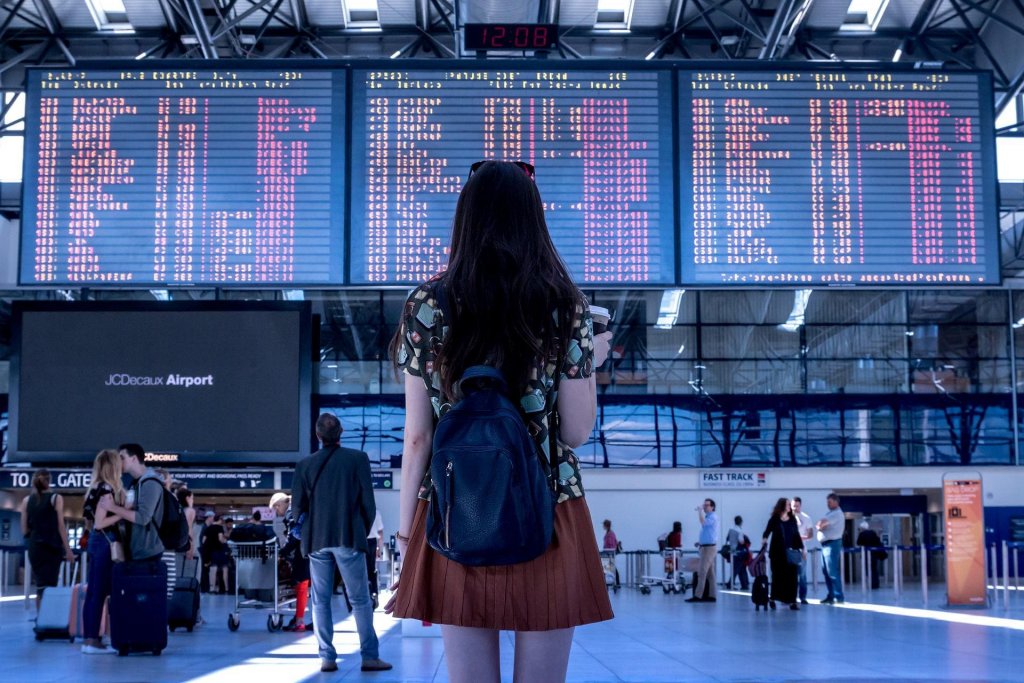 Mulher no aeroporto, de frente para um painel com informações sobre voos. Imagem disponível em Pixabay.