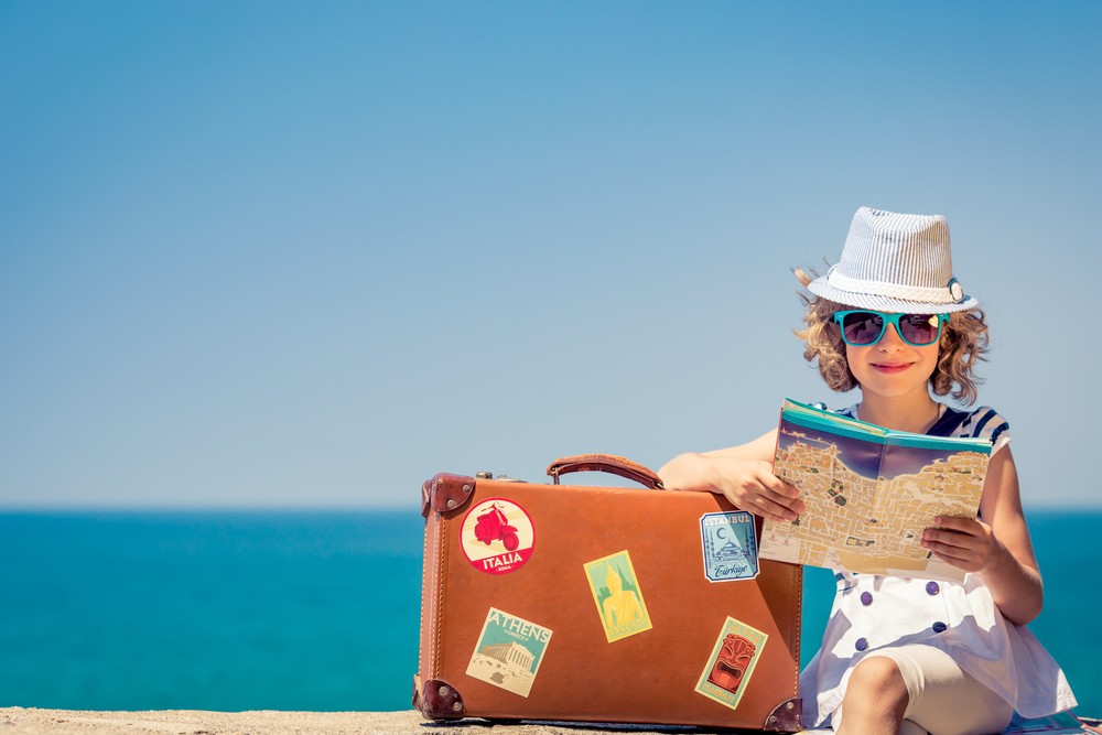 Criança olha mapa na praia com mala de viagem antiga