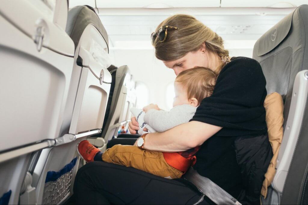 mulher e criança sentados na cadeira do avião. A criança está no colo da mulher, com um brinquedo na mão