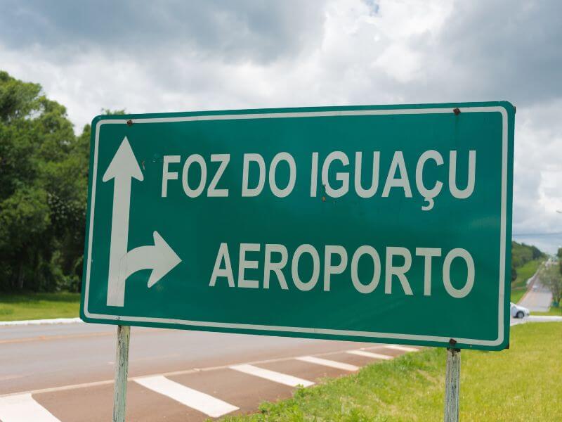 placa na estrada indicando que para chegar em foz do iguaçu é só seguir em frente, e para ir ao aeroporto é só virar a direita