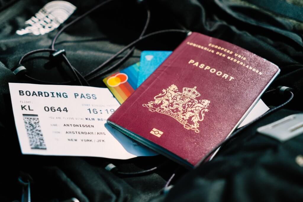 Passaporte de capa vermelha ao lado de uma passagem aérea. Imagem disponível em Unsplash.