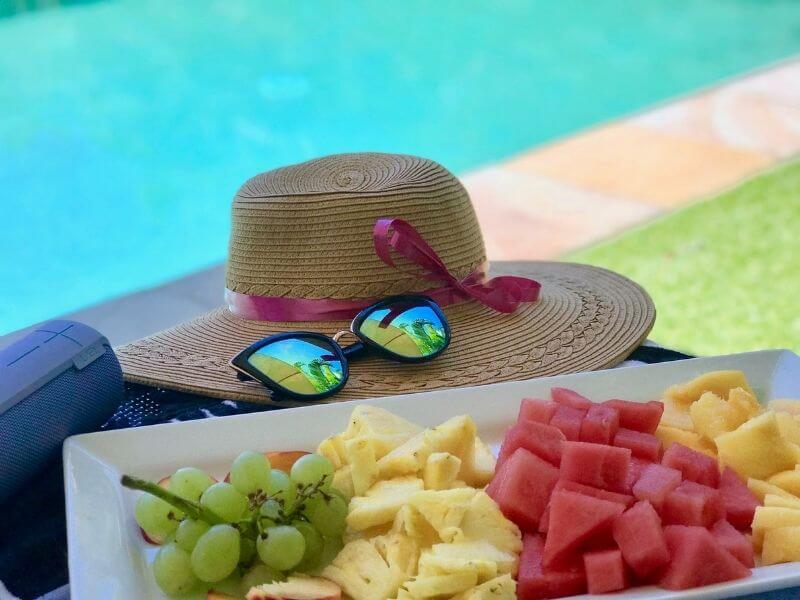 chapéu de praia na beira da piscina, com óculos escuros do lado e várias bandejas de frutas, imagem clássica de um resort all inclusive