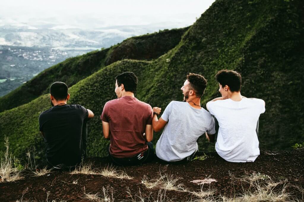 Homens sentados na natureza, de frente para montanha, rindo. Foto disponível no Unsplash