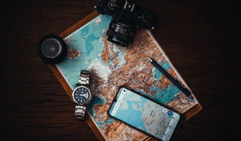um mapa estendido sobre a mesa, com um celular, relógio, câmera digital e caneta em cima
