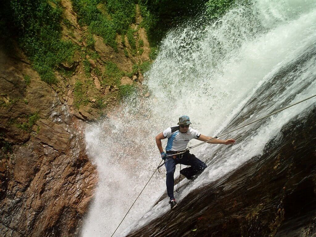 Homem fazendo turismo de aventura, em um rapel na cachoeira.