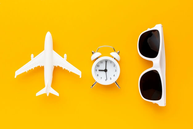 em um fundo amarelo estão uma réplica de um avião, um despertador e um par de óculos escuros na cor branca
