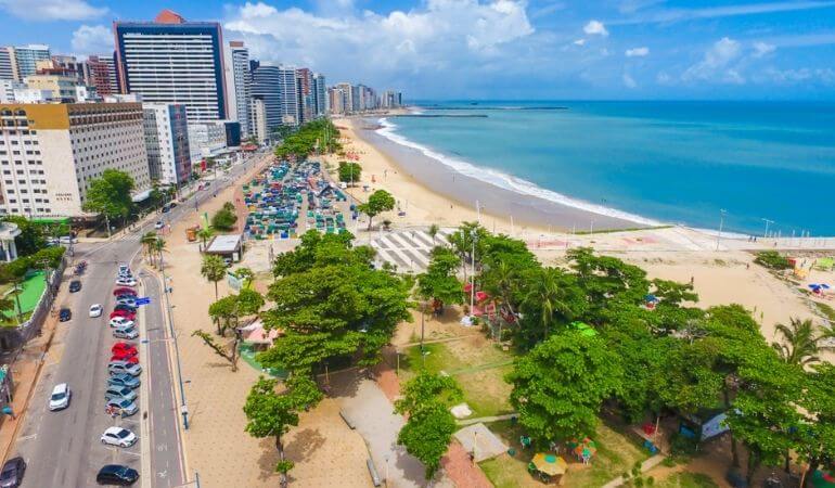 imagem aérea da cidade de fortaleza. Foto mostra avenida com prédios, ao lado da orla da praia