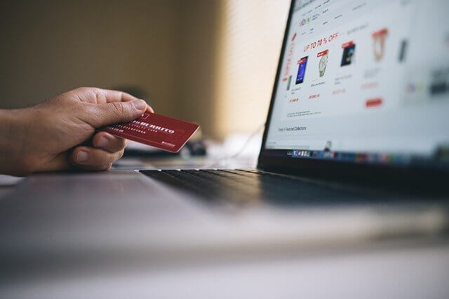 imagem ampliada de mão segurando cartão de crédito e tela de computador à frente