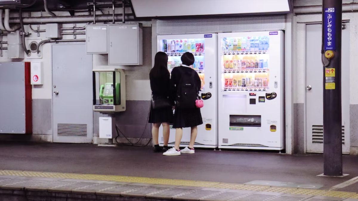 duas jovens estudantes japonesas em frente a uma máquina de vendas