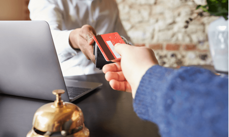 Recepção do hotel com funcionário e cliente passando o cartão de crédito na máquina