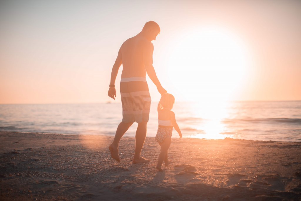 pai e filha andando na areia na beira do mar em um dos destinos incríveis para viagem de dia dos pais