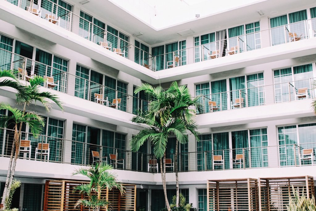 Foto da faichada de hotel, com palmeiras na frente. Imagem disponível no Unsplash