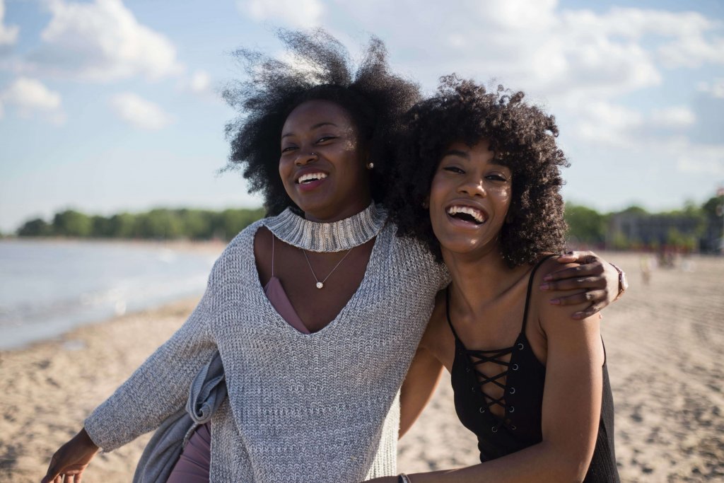 Duas mulheres negras, abraçadas, na praia.