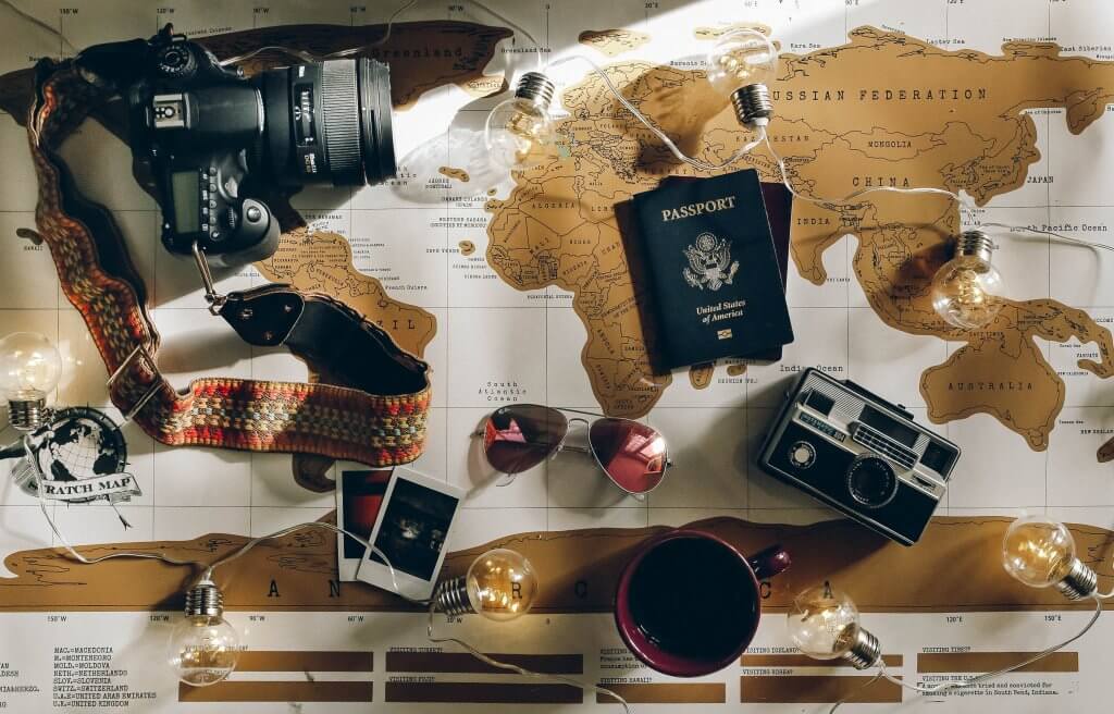 Mapa-múndi com óculos escuro, câmera e passaportes em cima. Imagem disponível no Unsplash