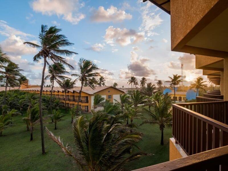 Vista da área externa do Makai Resort em Aracaju, com gramado, árvores e palmeiras e o mar ao fundo