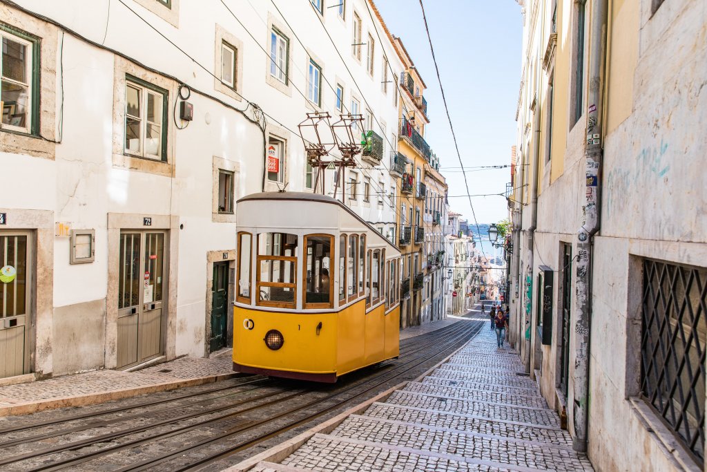 Bondinho branco com amarelo anda por uma rua antigas de Lisboa. Imagem disponível em Unsplash.