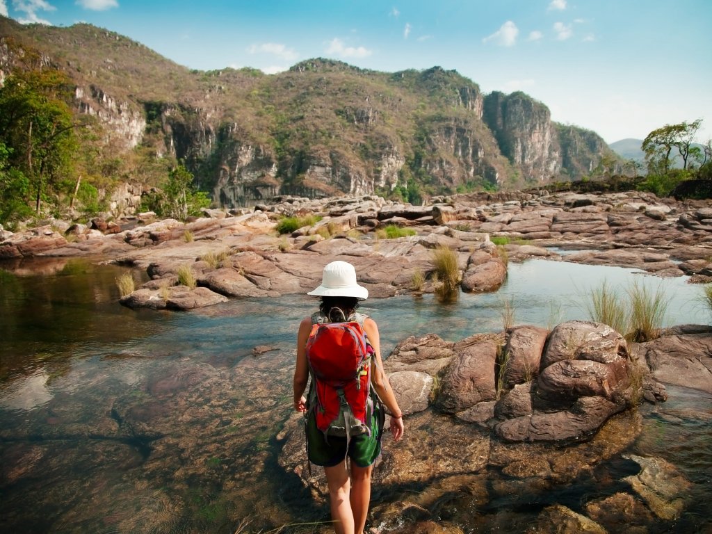 Mulher, de mochila nas costas, caminha sobre pedras. Imagem disponível em Shutterstock