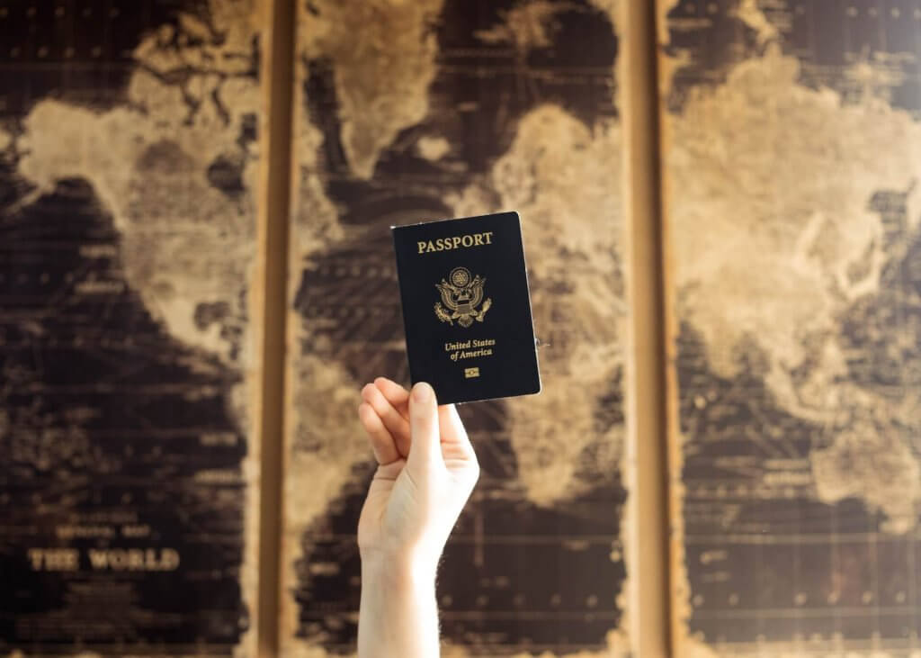 Pessoa após renovar o passaporte segurando-o no alto na frente de um mapa