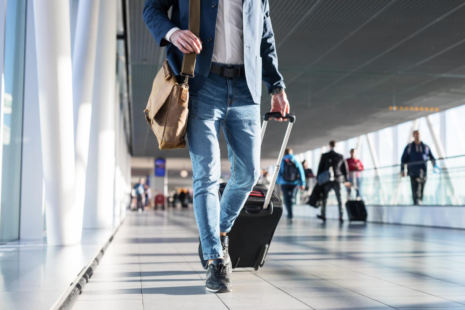 Homem caminha carregando uma mala no hall do aeroporto. Imagem disponível em Shutterstock.