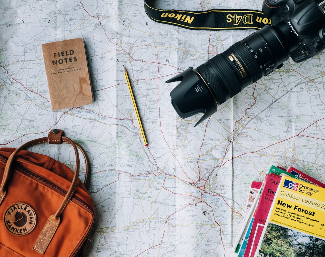 Câmera fotográfica, mochila, lápis e guias em cima de um mapa.