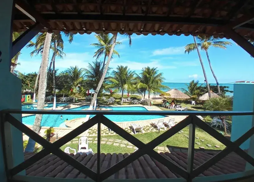 Área de lazer com piscina e coqueiros no Albacora Praia Hotel